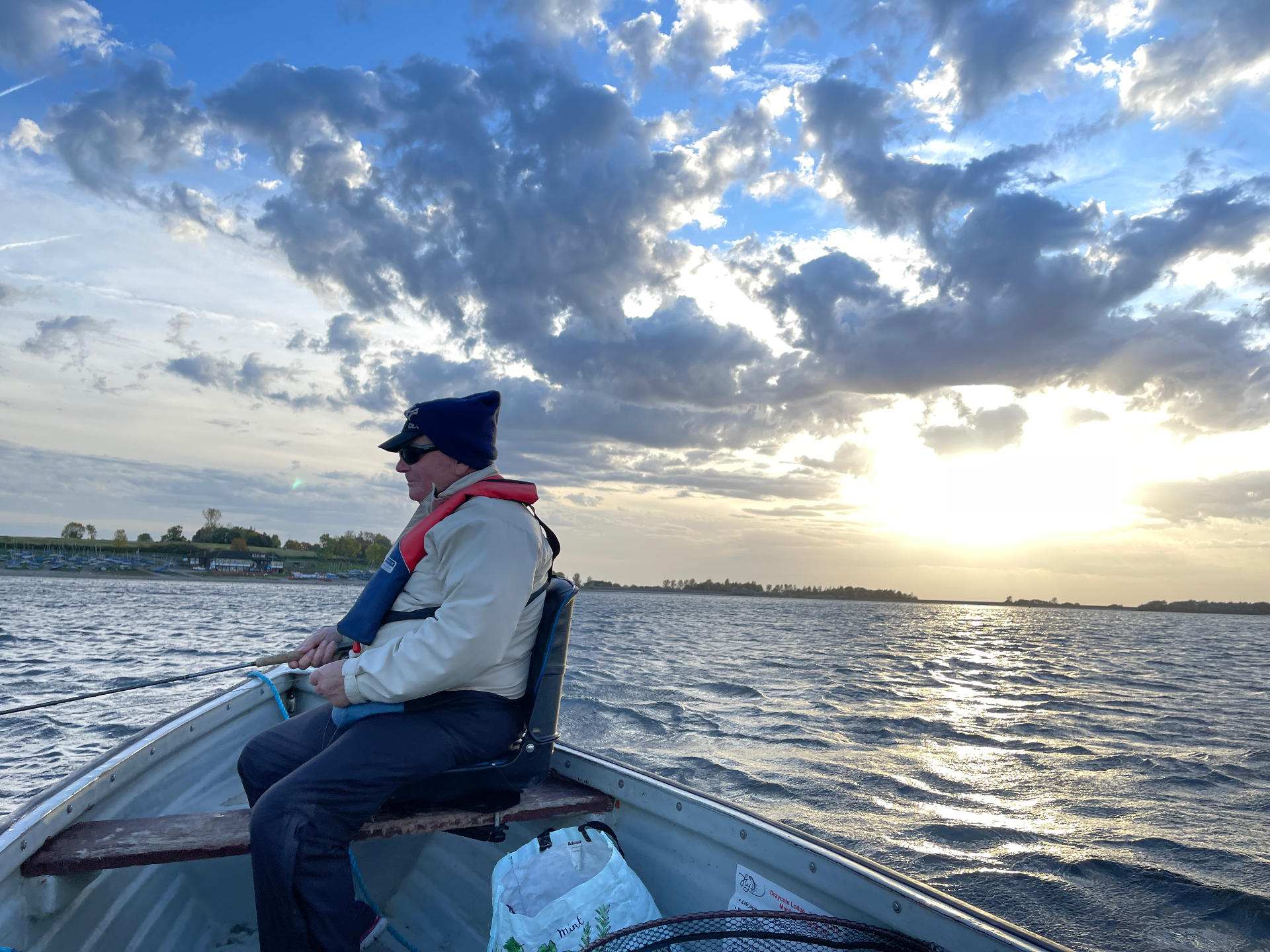 An angler in a boat fly fishing a reservoir under a dramatic sky at sunset