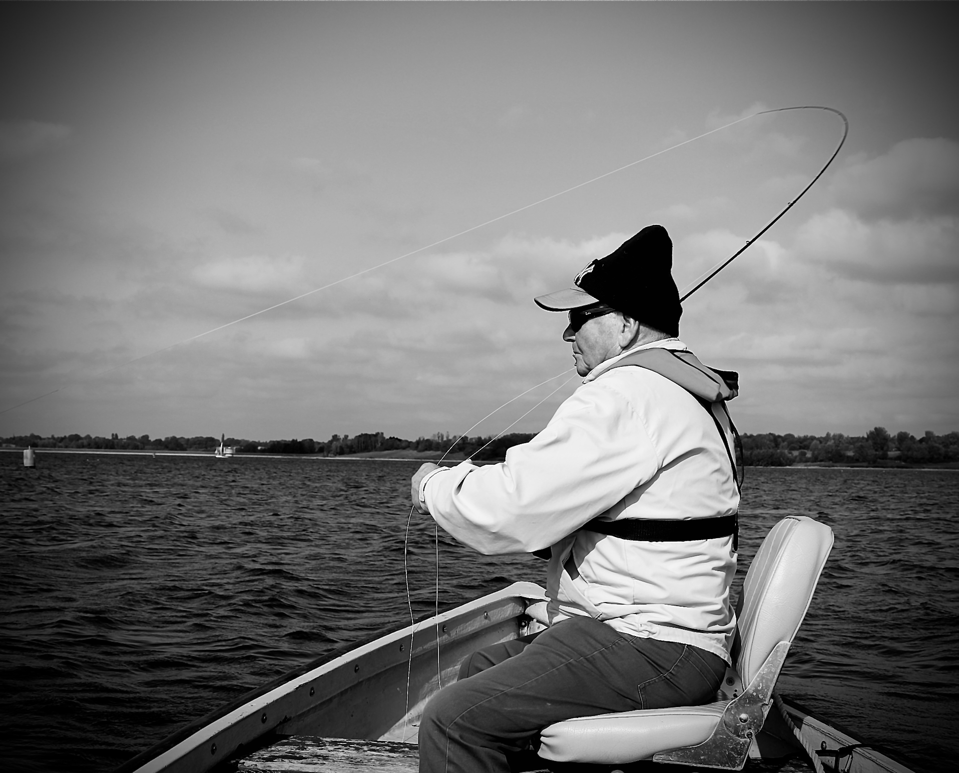 An older angler casting a fly line from a boat on a windswept reservoir
