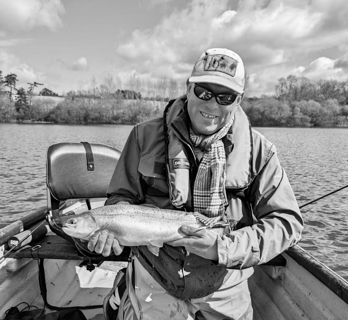 A smiling angler in a boat holding a rainbow trout