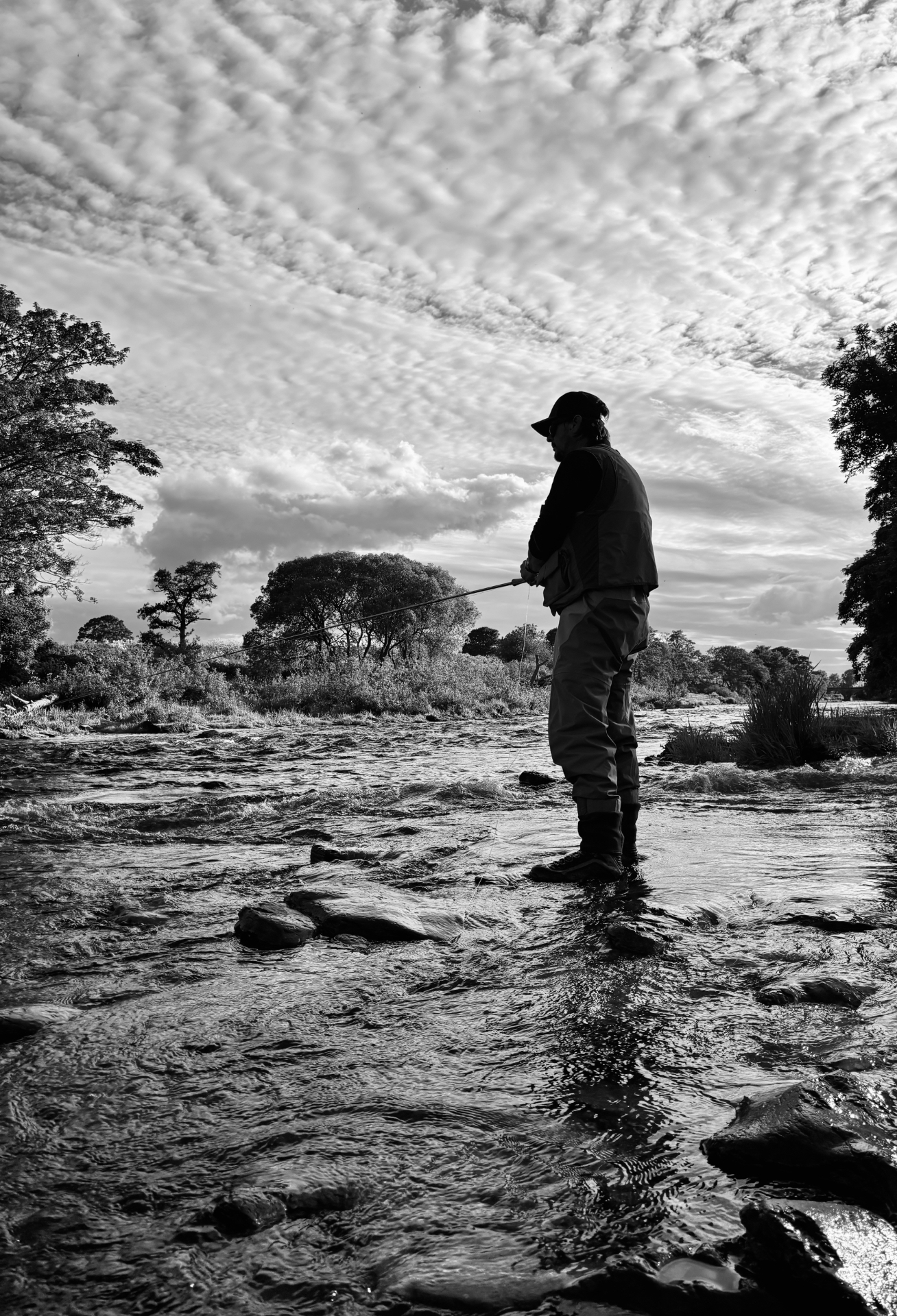 An angler silhouetted mid-river beneath a rippled sky