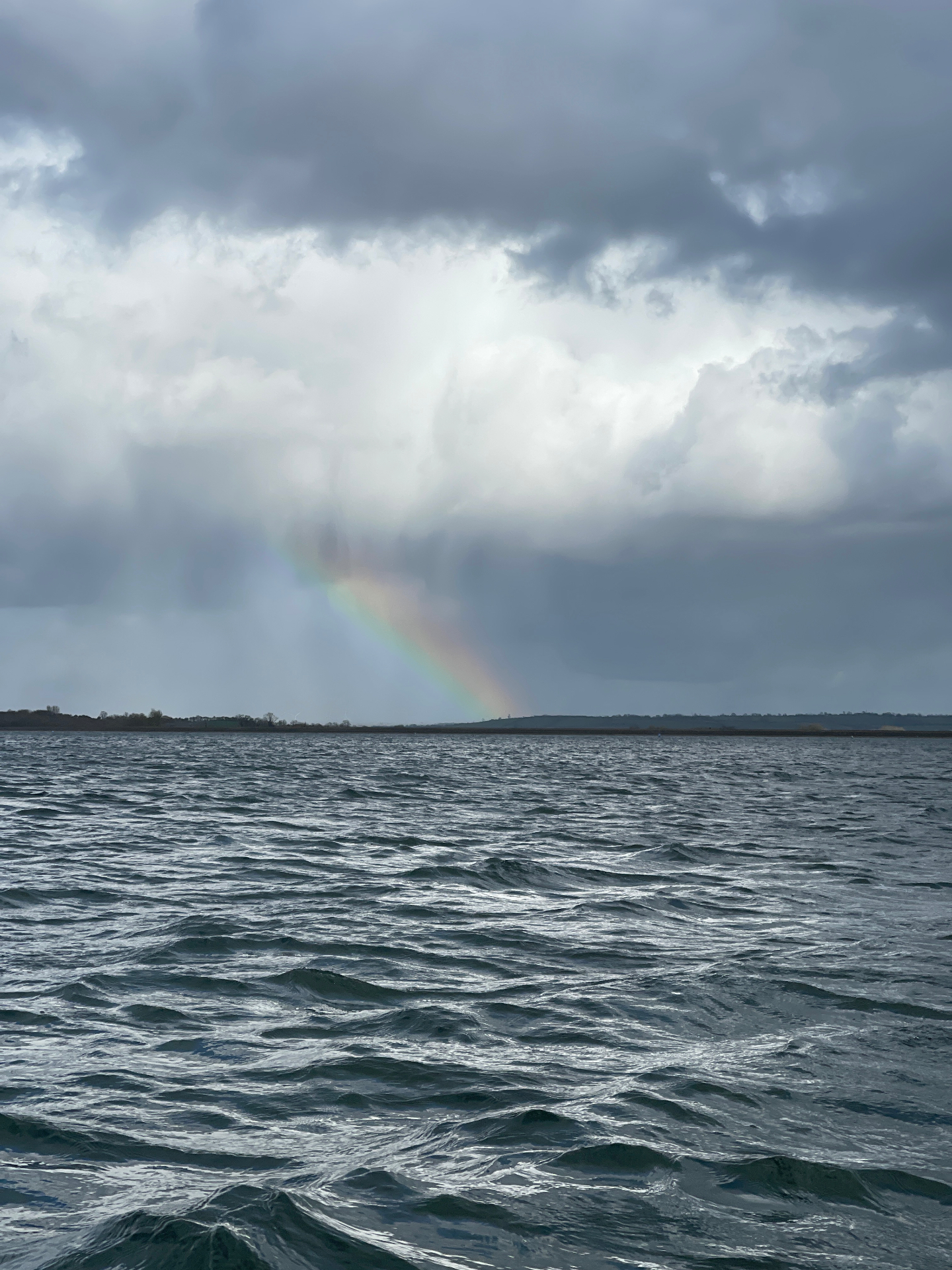 A rainbow over choppy grey water under storm clouds