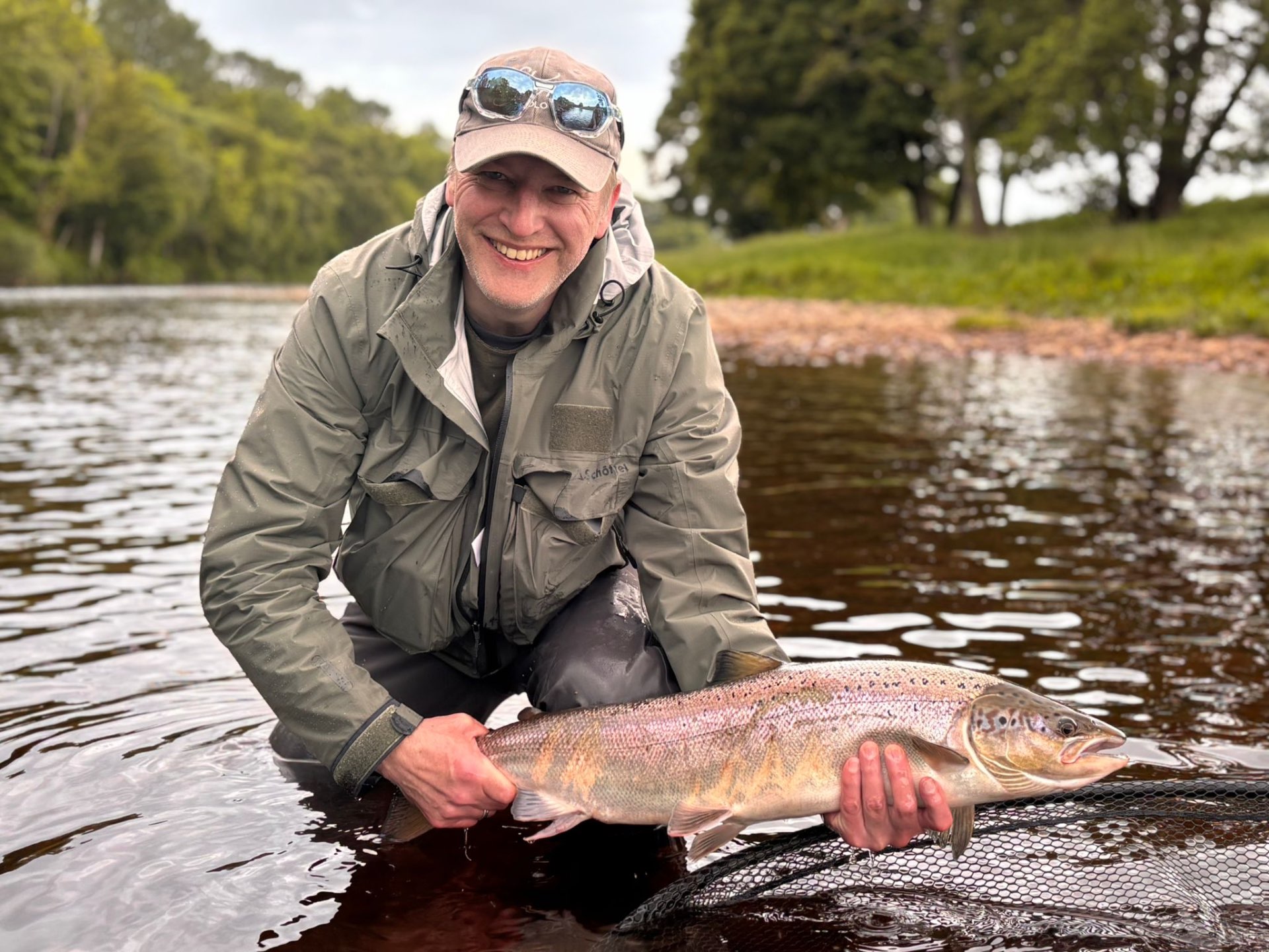 A smiling angler kneeling in a river holding a salmon before release